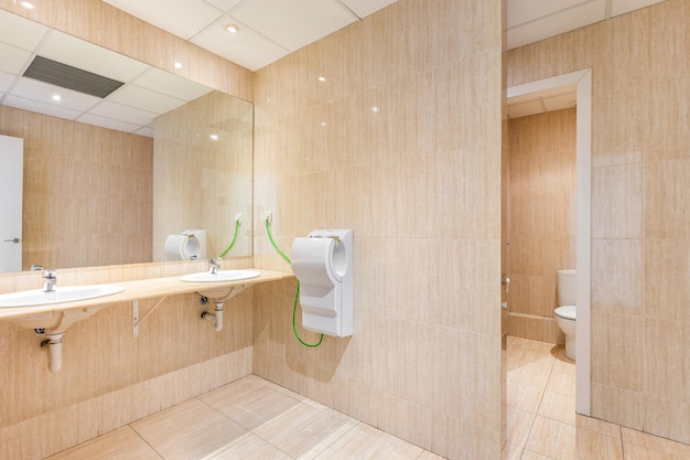 Banheiro público com espelho grande, lava-mãos, secadora e portas de banheiro