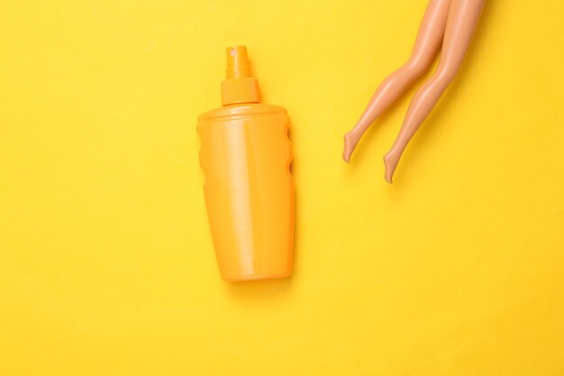 Banhos de sol nas férias de verão Creme solar e pernas de boneca em um fundo amarelo Minimalismo Flat lay