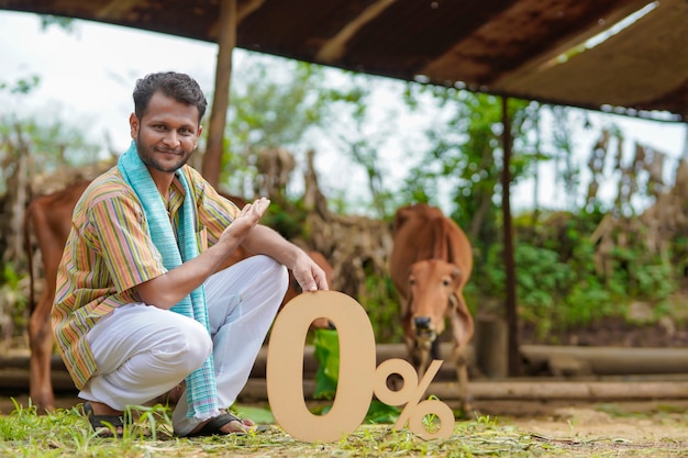 Bank- oder Finanzkonzept: Junger indischer Bauer, der auf seiner Rinderfarm ein Null-Prozent-Symbol zeigt