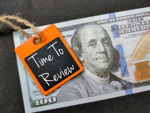 Banknoten und farbiges Holzbrett mit dem Wort Time to Review auf schwarzem Hintergrund