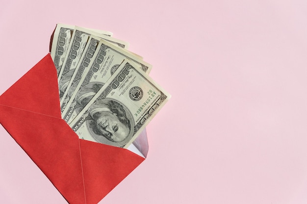 Banknoten von 100 Dollar in einem roten Umschlag auf einem rosa Hintergrund. Umschlag mit der Inschrift Ersparnisse und Dollarnoten. Verwalten Sie Ihre Finanzen und sparen Sie Geld Konzept. Speicherplatz kopieren