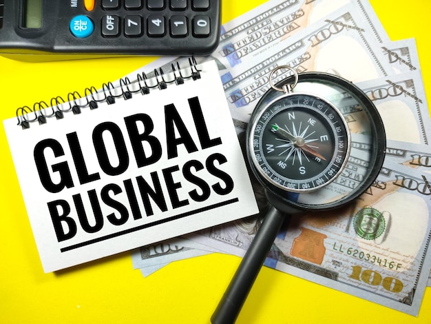 Banknotenkompass und Lupe mit Text GLOBAL BUSINESS auf gelbem Hintergrund