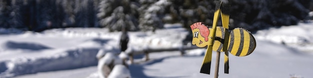 Banner 41 mit einer Wetterfahne in Form einer fröhlichen Biene vor dem Hintergrund von Bergen und einem dichten Fichtenwald in Bokeh