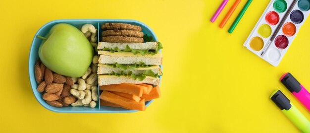 Foto banner almuerzo escolar en la caja azul y papelería escolar en el fondo amarillo vista superior espacio de copia