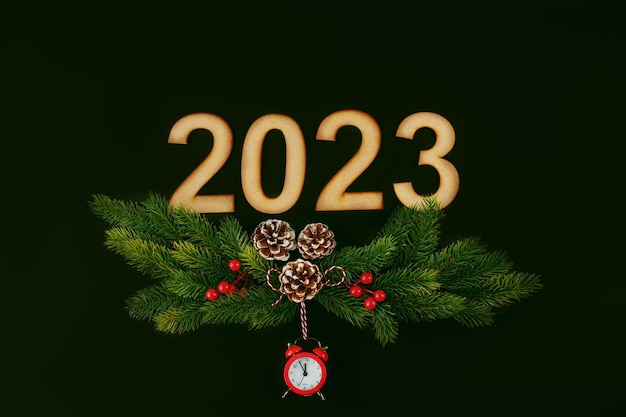 Banner de Año Nuevo con números de madera 2023 ramas de árboles de Navidad piñas y despertador rojo