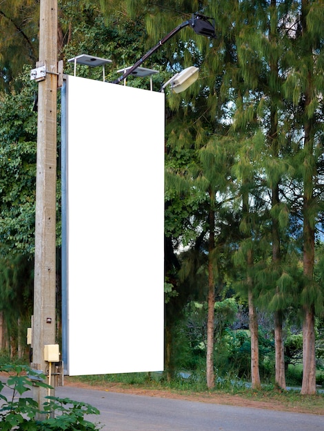 Banner en blanco blanco vacío en poste eléctrico para publicidad al lado de la carretera cerca del árbol y jardín verde