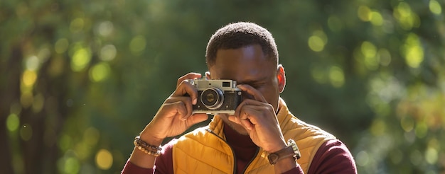 Banner chico afroamericano fotógrafo tomando fotos con una cámara vintage en el parque verde de la ciudad diversidad de actividades de ocio y concepto de hobby