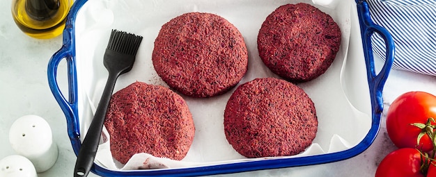 Banner de chuletas veganas crudas para hamburguesa sin carne en una bandeja para hornear sobre una mesa