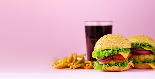 Banner de comida rápida. Las hamburguesas jugosas de la carne, las patatas de las patatas fritas y la cola beben en fondo rosado. Comida para llevar. Concepto de dieta poco saludable