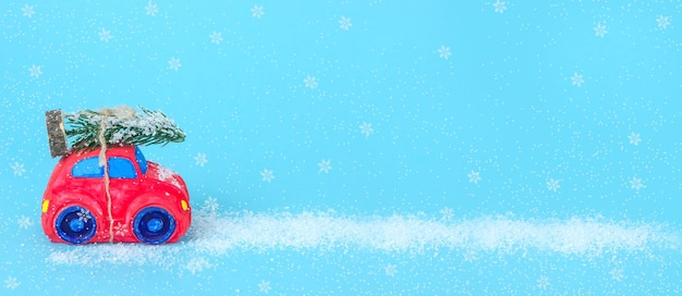 Foto banner de fundo azul com carro vermelho com árvore de natal coberta de neve com espaço de cópia