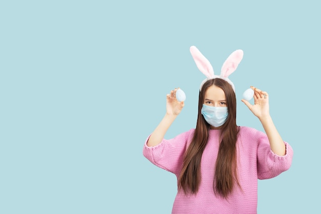 Banner de Páscoa com espaço para cópia menina adolescente com ovos de Páscoa em uma máscara médica em um fundo azul