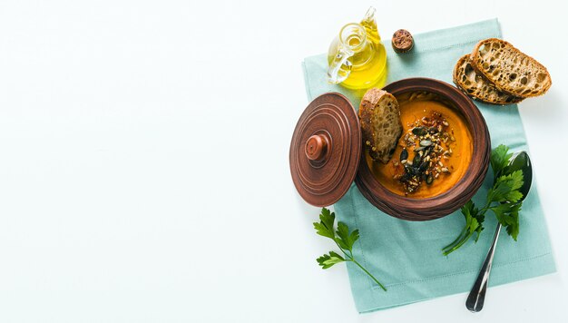 Banner de sopa de abóbora com sementes e pão de centeio fresco em uma tigela de barro na mesa