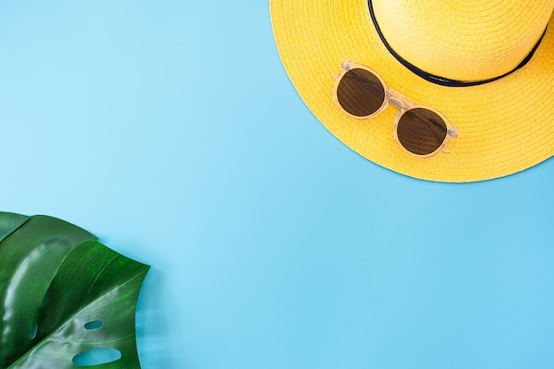 Foto banner de verão azul com chapéu amarelo, óculos escuros e folha de monstera em azul