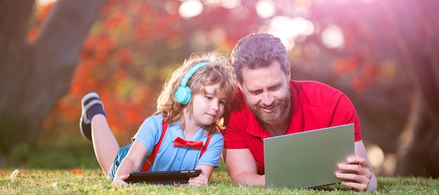 Banner do pai no filho da escola com laptop estudo on-line deitado na grama educação on-line no laptop pai e filho usam tecnologia de comunicação moderna no parque