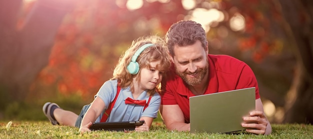 Banner do pai no filho da escola com laptop estudo on-line deitado na grama família feliz de pai e filho usa laptop para videochamada ou lição de comunicação moderna