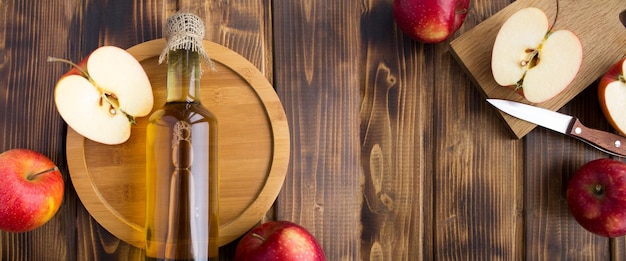Banner Draufsicht auf Apfelessig in der Glasflasche und rote Äpfel auf dem Holzhintergrund Kopierbereich
