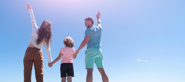 Banner de familia abrazándose en la playa del mar Banner horizontal de vacaciones familiares de verano Familia de madre padre y niño mirando en el futuro tomados de la mano en la vista posterior de verano