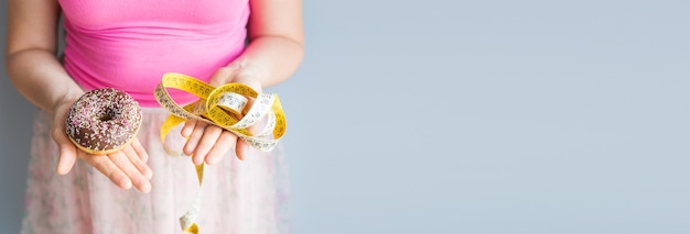 Banner fechado das mãos da mulher segurando uma rosquinha e uma fita métrica O conceito de alimentação saudável Dieta espaço para cópia