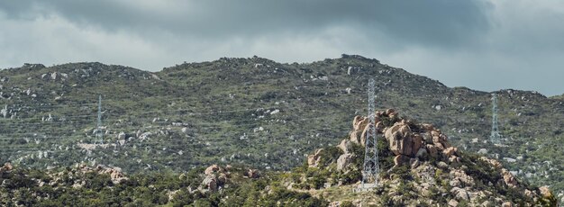 BANNER Floresta verde montanha rochosa com vista para a bela paisagem natural Cumulus dramáticas nuvens tempestuosas Pólos de alta tensão eletricidade energia em lugares selvagens remotos planeta