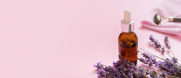 Banner con frasco cuentagotas y masajeador de piel facial con flores de lavanda sobre fondo de color