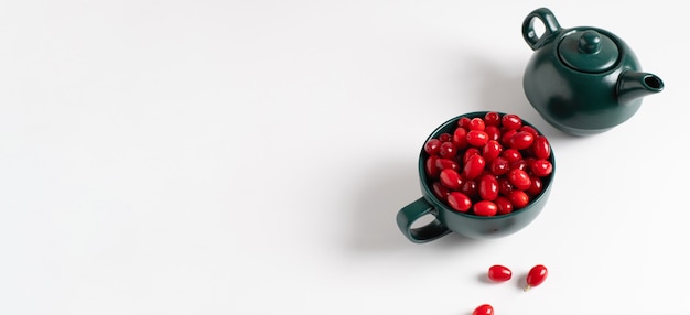 Foto banner, frutos rojos maduros de cornejo en un plato verde sobre un fondo blanco.