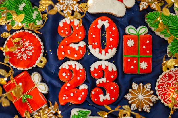 Banner für Weihnachten und Neujahr Lebkuchen Zahlen 2023 Schneeflocken Weihnachtsmütze Weihnachtsbäume Girlanden auf blauem Seidenstoff Hintergrund