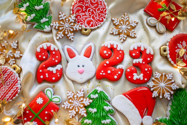 Banner für Weihnachten und Neujahr Lebkuchen Zahlen 2023 Schneeflocken Weihnachtsmütze Weihnachtsbäume Girlanden auf weißem Seidenstoff Hintergrund Lebkuchen-Kaninchen-Symbol Chinesischer Tierkreiskalender