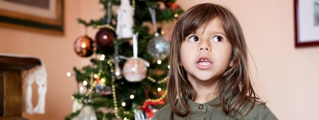 Banner horizontal o plantilla con una linda niña recitando el poema de Navidad en la sala de estar frente al árbol de Navidad Concepto de vacaciones de Navidad e infancia