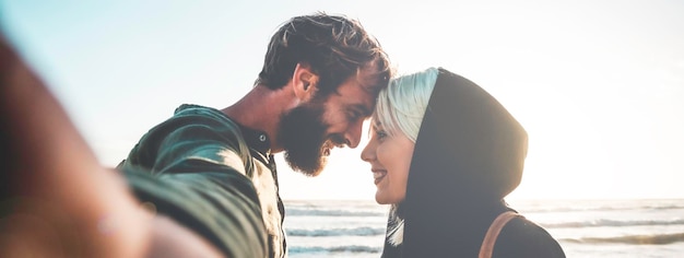 Banner horizontal ou cabeçalho com casal apaixonado tomando selfie na praia ao pôr do sol Mulher com olhar magnético e seu namorado hipster olhando nos olhos enquanto eles tiram uma selfie