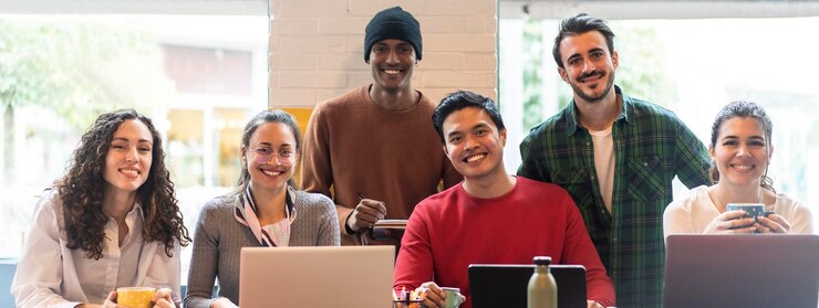Foto banner horizontal ou cabeçalho com colegas de trabalho multiétnicos sorridente olhando para a câmera fazendo foto de equipe em um escritório moderno juntos grupo de trabalho ou departamento diversificado rindo posando para foto no local de trabalho