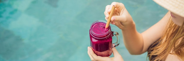 Banner langformatige junge Frau, die Drachenfrucht-Smoothies auf dem Hintergrund der Poolfrucht trinkt