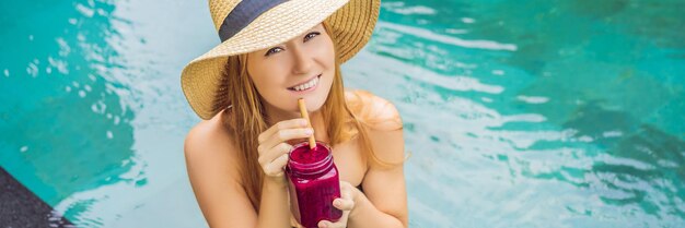 Banner langformatige junge Frau, die Drachenfrucht-Smoothies auf dem Hintergrund der Poolfrucht trinkt