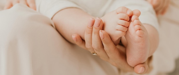 Banner Mãe amorosa segurando nas mãos os pés do bebê recém-nascido Pés do bebê nas mãos da mãe Pés minúsculos do bebê recém-nascido nas mãos femininas closeup Mãe e seu filho Conceito de família feliz