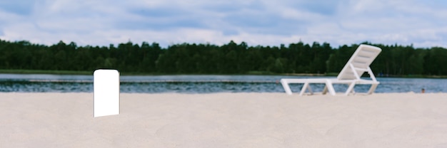 Banner, maqueta de Smartphone en la arena de la playa. Con el telón de fondo de una tumbona, agua y árboles. Concepto sobre el tema de los viajes.