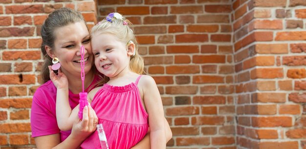 Foto banner menina loira com implante coclear brincando com sua mãe ao ar livre com deficiência auditiva surda