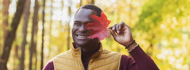 Banner Nahaufnahme Porträt eines lustigen afroamerikanischen Mannes, der sein Gesicht mit Herbstahornblatt bedeckt