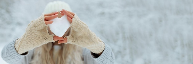 Banner Nahaufnahme Schnee Herz in Händen in Strickhandschuhen auf dem Hintergrund der Schneedecke Valentinstag