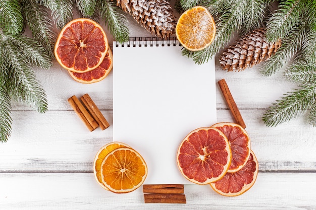 Banner navideño con árbol verde, conos, naranja, canela y cuaderno.