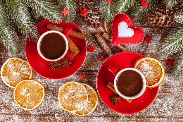 Banner navideño con árbol verde, conos, tazas rojas con chocolate caliente, naranja y canela.