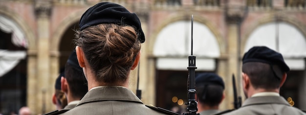 Banner o encabezado horizontal con mujeres uniformadas de pie durante la ceremonia militar en Bolonia Italia En primer plano, una mujer vista desde atrás con un rifle de bayoneta