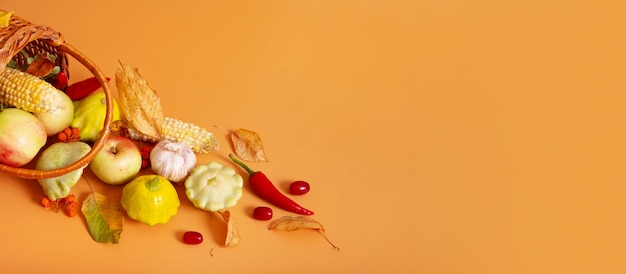 Banner de otoño con canasta de cosecha con maíz, manzanas, calabacín y pimientos sobre un fondo naranja Concepto de cosecha