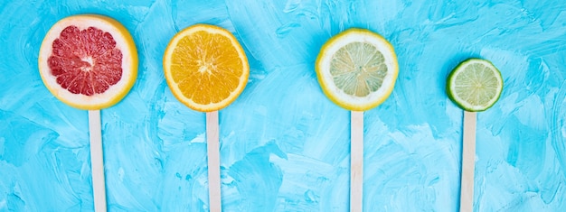 Banner de paletas de rodajas de cítricos sobre un fondo azul.