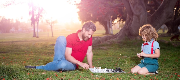 Banner de papá e hijo juegan juego de lógica de ajedrez padre e hijo jugando ajedrez en el césped en los padres del parque