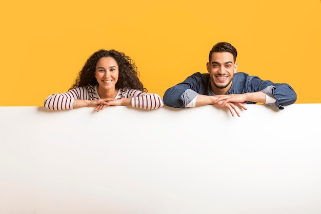 Banner publicitario Sonriente pareja árabe apoyándose en el tablero de anuncios blanco en blanco