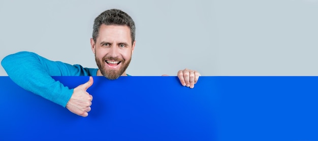 Foto banner de retrato de cara de hombre con producto de espacio de copia que presenta información de novedad masculino detrás de papel azul mostrar pulgar hacia arriba