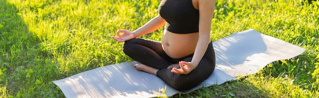 Banner schwangere Frau meditiert, während sie auf einer Yogamatte auf dem Rasen sitzt, sonniger Sommerabend, Kopienraum Konzept der Befriedung und des Energieschubs