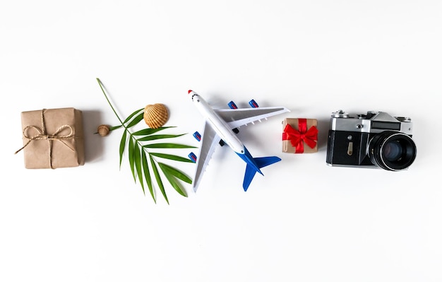 Banner de verano con una cámara, una hoja de palma, un avión, conchas, un regalo sobre un fondo blanco. Concepto de vacaciones tropicales.