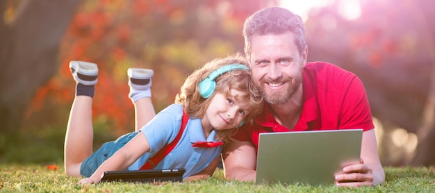 Banner von Vater auf Sohn Schuljunge mit Laptop studieren online auf Gras liegend Online-Bildung auf Laptop Vater und Sohn nutzen moderne Kommunikationstechnologie