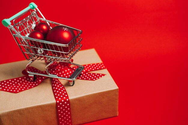 Banner web de compras de venta de navidad con mini carro con caja de regalo y bolas rojas de adornos de navidad