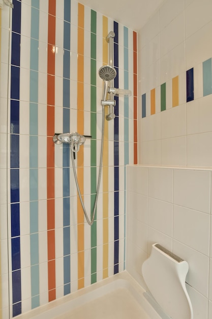 Foto un baño con azulejos coloridos en la pared y un cabezal de ducha montado a la pared frente a un inodoro blanco